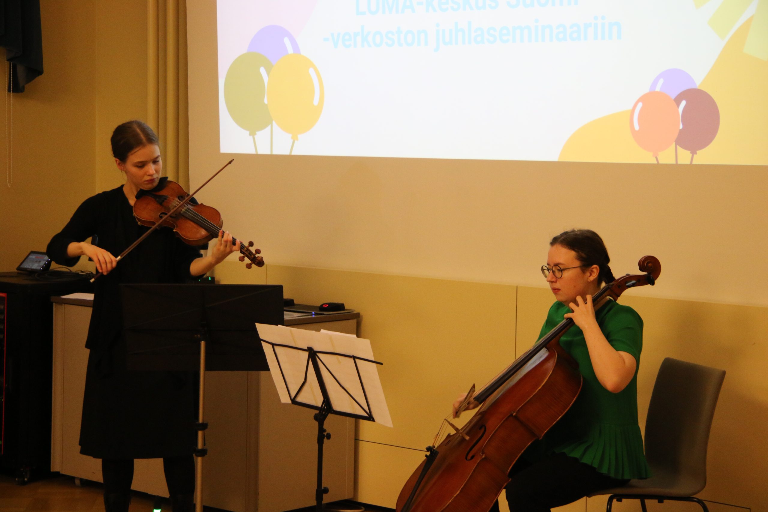 Två unga kvinnor som spelar instrument. En av dem spelar cello ch den andra spelar violin.